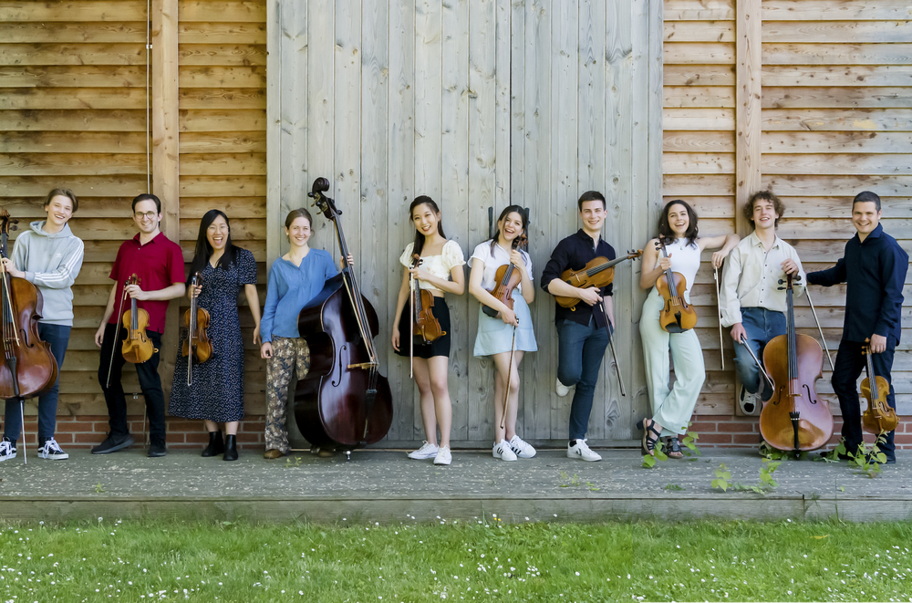 Junge klassische Musiker mit ihren Instrumenten vor einem Gebäude aus Holz